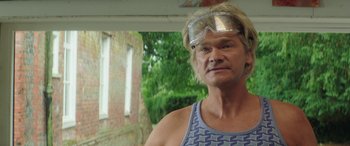 Movie still from “Mindhorn” (2016), directed by Sean Foley – A man wearing goggles standing in front of a brick building; Close Up shot, Low angle
