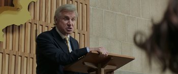 Movie still from “Mindhorn” (2016), directed by Sean Foley – A man in a suit and tie is speaking at a lectern; Close Up shot, Low angle
