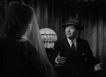Movie still from “Ministry of Fear” (1944), directed by Fritz Lang – A man in a suit talking to a woman in a hat; Medium shot, Over the shoulder angle