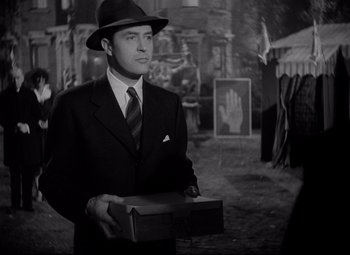 Movie still from “Ministry of Fear” (1944), directed by Fritz Lang – A black and white photo of a man in a suit and hat holding a box; Medium shot, Over the shoulder angle