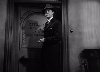Movie still from “Ministry of Fear” (1944), directed by Fritz Lang – A man in a suit and hat standing in front of a building; Medium shot, Low angle