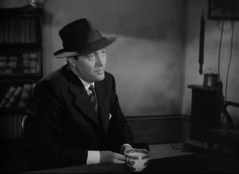 Movie still from “Ministry of Fear” (1944), directed by Fritz Lang – A black and white photo of a man sitting at a table with a coffee cup; Medium shot, Low angle