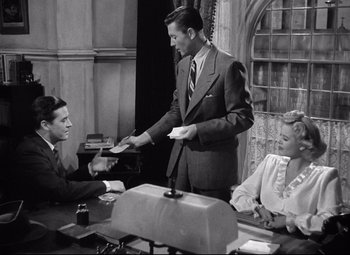 Movie still from “Ministry of Fear” (1944), directed by Fritz Lang – A black and white photo of a man handing a card to a woman; Medium shot, High angle