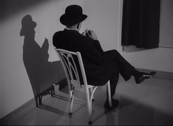 Movie still from “Ministry of Fear” (1944), directed by Fritz Lang – A man sitting on top of a white chair in front of a window; Medium shot, High angle