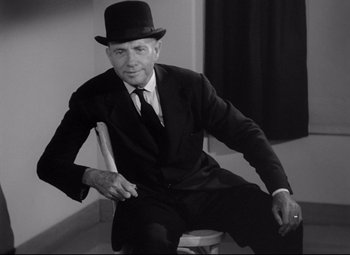 Movie still from “Ministry of Fear” (1944), directed by Fritz Lang – A man sitting on a chair wearing a suit and a hat; Medium shot, Low angle