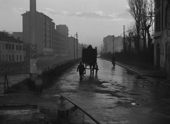 Movie still from “Miracle in Milan” (1951), directed by Vittorio De Sica – A black and white photo of a street scene with people walking on the sidewalk; Wide shot, Low angle