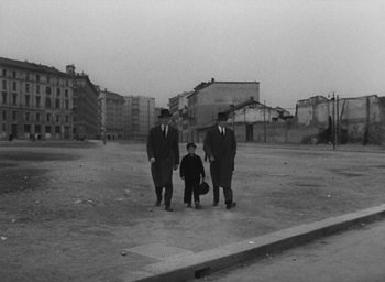 Movie still from “Miracle in Milan” (1951), directed by Vittorio De Sica – A group of men standing next to each other in an empty lot; Wide shot, High angle