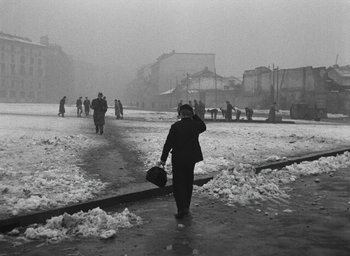 Movie still from “Miracle in Milan” (1951), directed by Vittorio De Sica – A man walking down a snowy street holding a suitcase; Wide shot, High angle