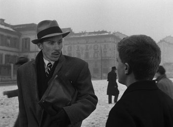 Movie still from “Miracle in Milan” (1951), directed by Vittorio De Sica – A man wearing a hat talking to another man in a suit; Medium shot, Over the shoulder angle