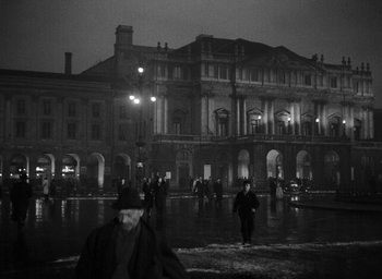 Movie still from “Miracle in Milan” (1951), directed by Vittorio De Sica – People walking in the rain in front of an old building; Extreme Wide shot, Low angle