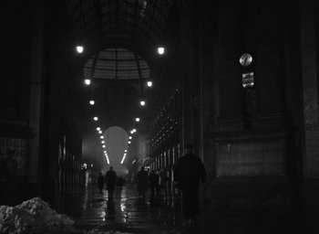 Movie still from “Miracle in Milan” (1951), directed by Vittorio De Sica – People are walking through a dark hallway with lights; Extreme Wide shot, Low angle
