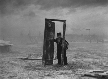 Movie still from “Miracle in Milan” (1951), directed by Vittorio De Sica – A man standing next to an open door in the middle of a field; Wide shot, High angle