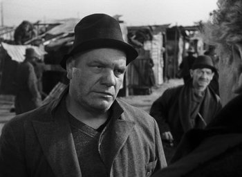 Movie still from “Miracle in Milan” (1951), directed by Vittorio De Sica – An older man wearing a hat in a black and white photo; Close Up shot, Over the shoulder angle
