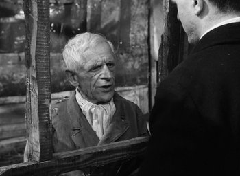 Movie still from “Miracle in Milan” (1951), directed by Vittorio De Sica – An older man looking in the mirror while standing next to another man; Medium shot, Over the shoulder angle