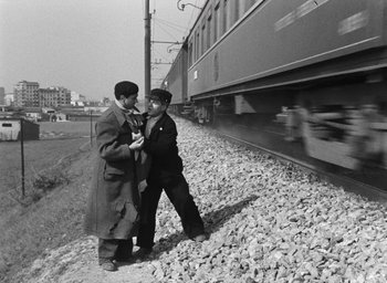Movie still from “Miracle in Milan” (1951), directed by Vittorio De Sica – Two men standing next to each other near a train track; Wide shot, Over the shoulder angle