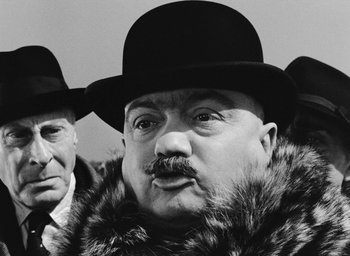 Movie still from “Miracle in Milan” (1951), directed by Vittorio De Sica – A man in a fur coat wearing a hat and a fur coat; Close Up shot, Over the shoulder angle