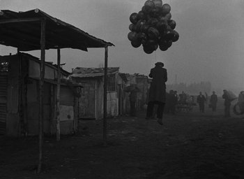 Movie still from “Miracle in Milan” (1951), directed by Vittorio De Sica – A man flying a bunch of balloons in the air; Wide shot, Low angle
