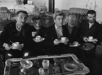 Movie still from “Miracle in Milan” (1951), directed by Vittorio De Sica – A group of men sitting around a table with cups; Medium shot, High angle