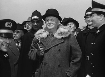 Movie still from “Miracle in Milan” (1951), directed by Vittorio De Sica – An old photo of a group of men in hats and coats holding microphones; Medium shot, Low angle