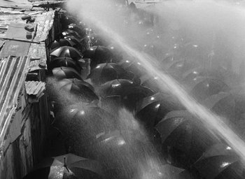 Movie still from “Miracle in Milan” (1951), directed by Vittorio De Sica – A bunch of umbrellas are being sprayed by a water cannon; Extreme Wide shot, High angle
