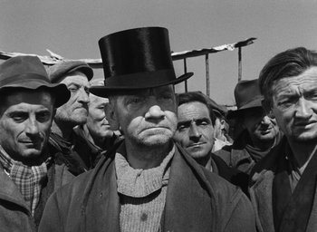 Movie still from “Miracle in Milan” (1951), directed by Vittorio De Sica – A group of men standing next to each other wearing hats; Medium shot, Low angle
