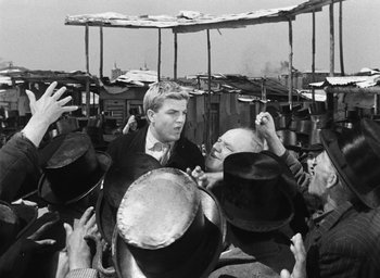 Movie still from “Miracle in Milan” (1951), directed by Vittorio De Sica – A group of people standing next to each other with hats on; Medium shot, High angle