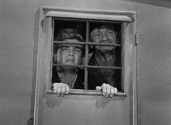 Movie still from “Miracle in Milan” (1951), directed by Vittorio De Sica – Two men looking out of a window through bars; Medium shot, Low angle