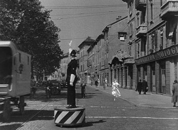 Movie still from “Miracle in Milan” (1951), directed by Vittorio De Sica – A man standing on a street corner holding a flag; Wide shot, Low angle