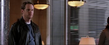 Movie still from “Miss Congeniality 2: Armed & Fabulous” (2005), directed by John Pasquin – A man in a leather jacket standing in front of a window; Medium shot, Over the shoulder angle