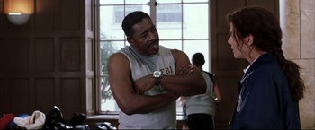 Movie still from “Miss Congeniality 2: Armed & Fabulous” (2005), directed by John Pasquin – A man in a grey shirt is holding his arm up; Medium shot, Low angle