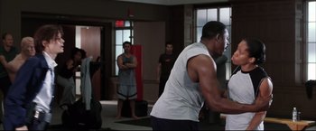 Movie still from “Miss Congeniality 2: Armed & Fabulous” (2005), directed by John Pasquin – A group of people in a room with a man in a gray shirt; Medium shot, Over the shoulder angle