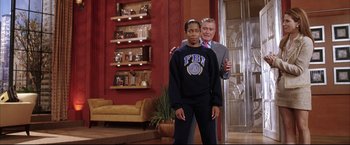 Movie still from “Miss Congeniality 2: Armed & Fabulous” (2005), directed by John Pasquin – A man standing next to a woman in front of a red wall; Medium shot, Over the shoulder angle