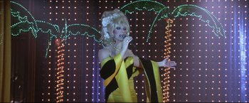 Movie still from “Miss Congeniality 2: Armed & Fabulous” (2005), directed by John Pasquin – A woman in a yellow and black dress is singing; Medium shot, Low angle