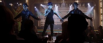 Movie still from “Miss Congeniality 2: Armed & Fabulous” (2005), directed by John Pasquin – A woman in a black dress and a blue hat on stage; Wide shot, Low angle