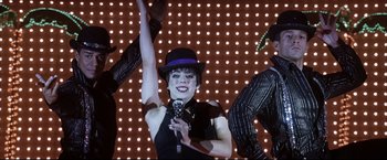 Movie still from “Miss Congeniality 2: Armed & Fabulous” (2005), directed by John Pasquin – A woman in a purple hat is holding a microphone; Medium shot, Low angle