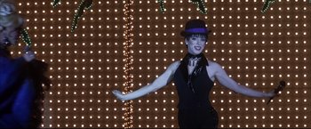 Movie still from “Miss Congeniality 2: Armed & Fabulous” (2005), directed by John Pasquin – A woman wearing a black dress and a purple hat; Medium shot, Low angle
