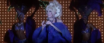 Movie still from “Miss Congeniality 2: Armed & Fabulous” (2005), directed by John Pasquin – A drag queen is singing into a microphone in front of a crowd; Medium shot, Low angle
