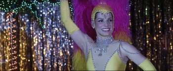 Movie still from “Miss Congeniality 2: Armed & Fabulous” (2005), directed by John Pasquin – A woman in a yellow dress and a pink and purple feathered headdress; Close Up shot, Low angle