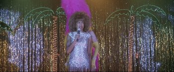 Movie still from “Miss Congeniality 2: Armed & Fabulous” (2005), directed by John Pasquin – A woman in a silver sequined dress holding a microphone; Medium shot, Over the shoulder angle