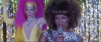Movie still from “Miss Congeniality 2: Armed & Fabulous” (2005), directed by John Pasquin – A woman in a silver dress is holding a microphone; Close Up shot, Low angle