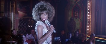 Movie still from “Miss Congeniality 2: Armed & Fabulous” (2005), directed by John Pasquin – A woman in a silver dress holding a microphone; Medium shot, Low angle