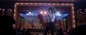 Movie still from “Miss Congeniality 2: Armed & Fabulous” (2005), directed by John Pasquin – A group of people on a stage with a microphone; Wide shot, Low angle