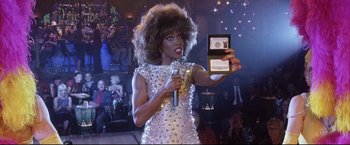 Movie still from “Miss Congeniality 2: Armed & Fabulous” (2005), directed by John Pasquin – A woman in a silver dress holding a microphone and taking a picture; Close Up shot, Overhead angle