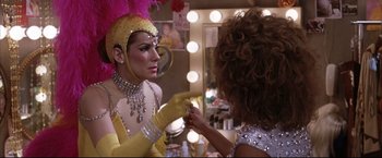 Movie still from “Miss Congeniality 2: Armed & Fabulous” (2005), directed by John Pasquin – A woman in a yellow and pink costume is looking in the mirror while another woman in a yellow and pink costume is holding a brush; Close Up shot, Over the shoulder angle