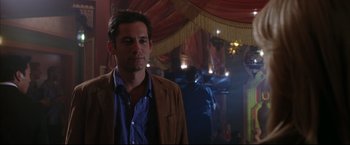 Movie still from “Miss Congeniality 2: Armed & Fabulous” (2005), directed by John Pasquin – A man in a brown jacket standing in a room; Medium shot, Over the shoulder angle
