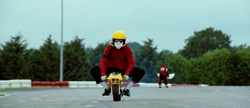 Movie still from “Mister Lonely” (2007), directed by Harmony Korine – A person riding a motorcycle on the street; Wide shot, Low angle