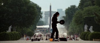Movie still from “Mister Lonely” (2007), directed by Harmony Korine – A woman in a black suit is holding a frisbee; Wide shot, Low angle