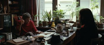 Movie still from “Mister Lonely” (2007), directed by Harmony Korine – A woman sitting at a desk with papers on it; Medium shot, Over the shoulder angle