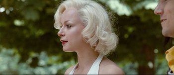 Movie still from “Mister Lonely” (2007), directed by Harmony Korine – A woman with blonde curly hair wearing a white halter top; Close Up shot, Over the shoulder angle