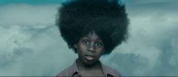 Movie still from “Mister Lonely” (2007), directed by Harmony Korine – A young boy with a large black afro in front of a cloudy sky; Close Up shot, Low angle
